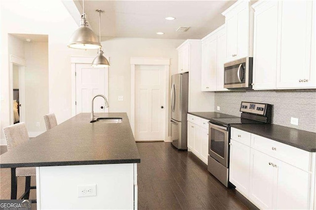 kitchen with dark countertops, a kitchen island with sink, a sink, and stainless steel appliances