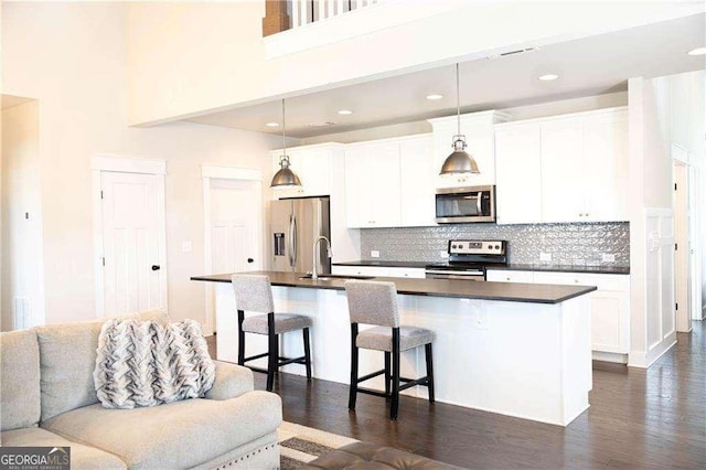 kitchen featuring a kitchen breakfast bar, dark countertops, white cabinets, a center island with sink, and stainless steel appliances