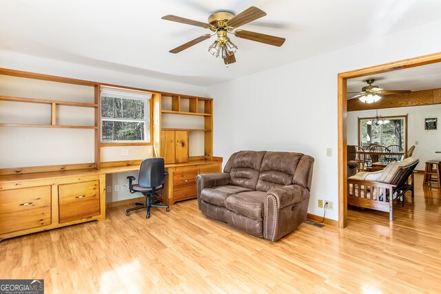home office with light wood finished floors, built in study area, and a ceiling fan