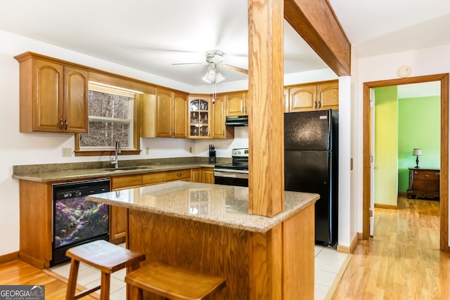 kitchen with light stone counters, a center island, black appliances, brown cabinets, and a sink