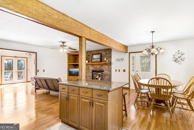 kitchen with light wood-type flooring, ceiling fan with notable chandelier, a fireplace, and a center island