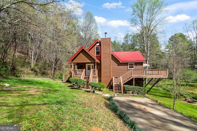 view of front of home featuring a front yard, faux log siding, metal roof, a chimney, and stairs