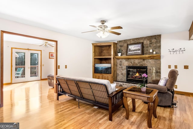 living room featuring a stone fireplace, ceiling fan, light wood finished floors, and baseboards