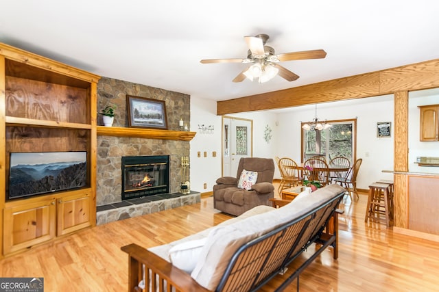 living area with a stone fireplace, wood finished floors, and ceiling fan with notable chandelier