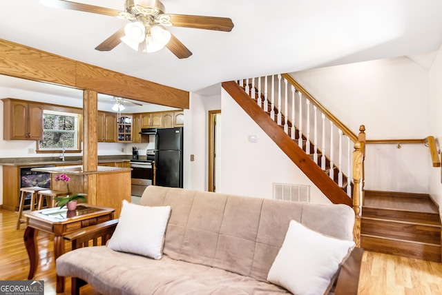 living area featuring light wood finished floors, a ceiling fan, visible vents, and stairs