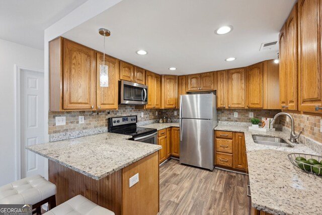 kitchen featuring stainless steel appliances, a sink, a peninsula, brown cabinetry, and recessed lighting