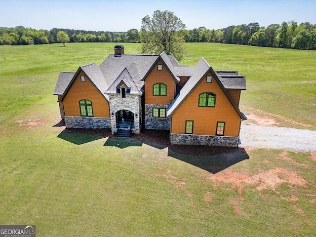 view of front of home featuring roof with shingles, a front lawn, stone siding, and a chimney