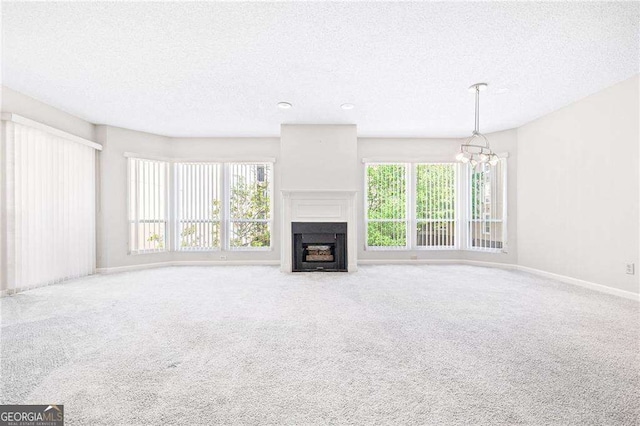 unfurnished living room featuring a textured ceiling, a chandelier, plenty of natural light, a fireplace with flush hearth, and carpet floors