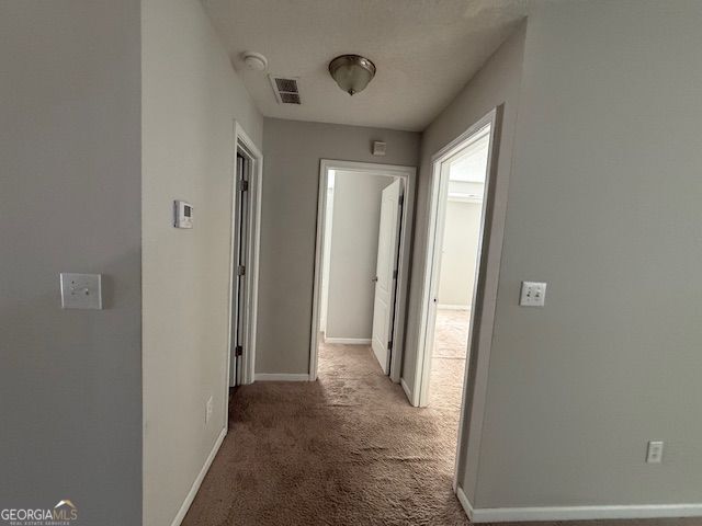 corridor with visible vents, light colored carpet, and baseboards