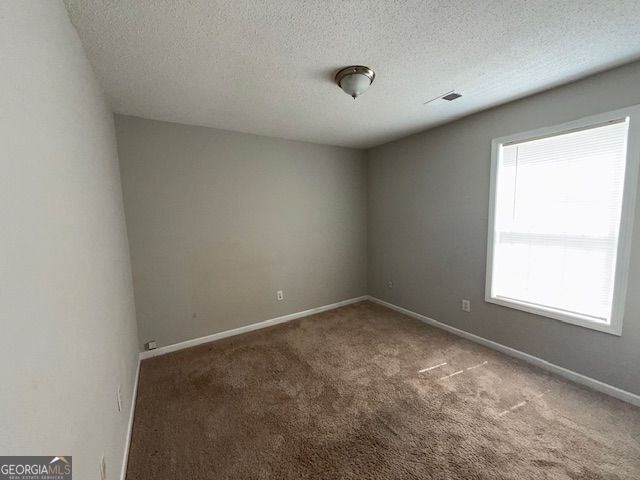 carpeted empty room with visible vents, baseboards, and a textured ceiling