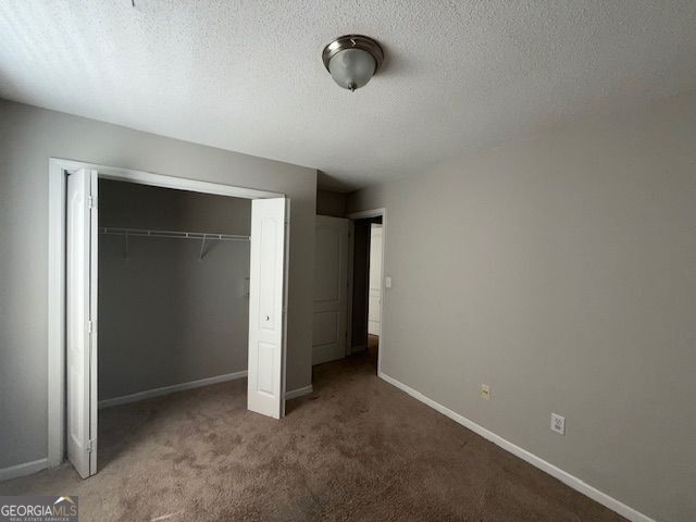 unfurnished bedroom featuring a textured ceiling, a closet, carpet flooring, and baseboards