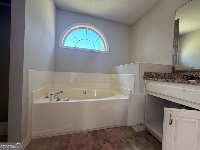 full bath featuring a textured ceiling, a garden tub, and vanity