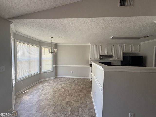 kitchen featuring visible vents, hanging light fixtures, black fridge, under cabinet range hood, and a textured ceiling