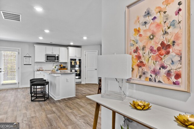 219 Rusty Plow Ln Unit 69, Perry, GA 31069 - kitchen with visible vents, appliances with stainless steel finishes, a kitchen breakfast bar, light wood-style floors, and white cabinetry