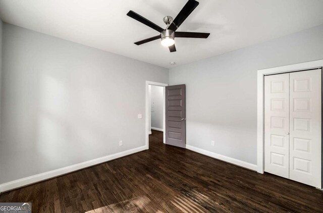 unfurnished bedroom featuring a closet, dark wood-style flooring, baseboards, and a ceiling fan