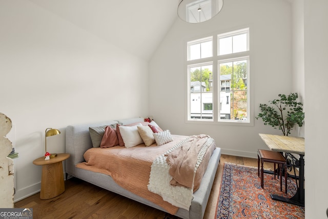 bedroom with wood finished floors, high vaulted ceiling, and baseboards