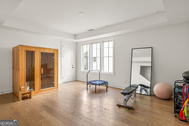 exercise room with a tray ceiling, baseboards, and wood finished floors