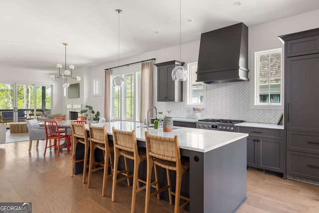 kitchen featuring custom range hood, gray cabinets, light wood finished floors, and decorative backsplash