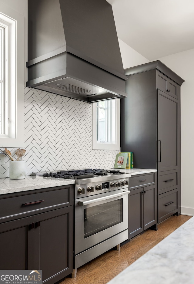 kitchen featuring light stone countertops, stainless steel range, custom range hood, gray cabinetry, and backsplash