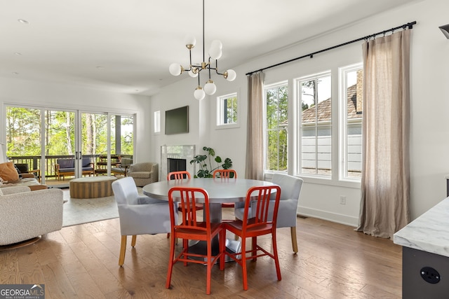 dining space with a wealth of natural light, an inviting chandelier, hardwood / wood-style flooring, and a fireplace