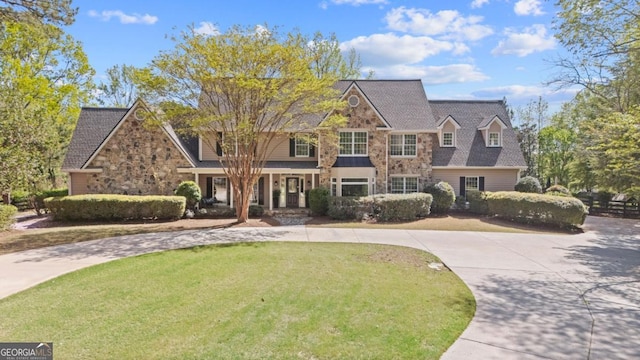 view of front of home featuring roof with shingles, curved driveway, a front yard, and stone siding