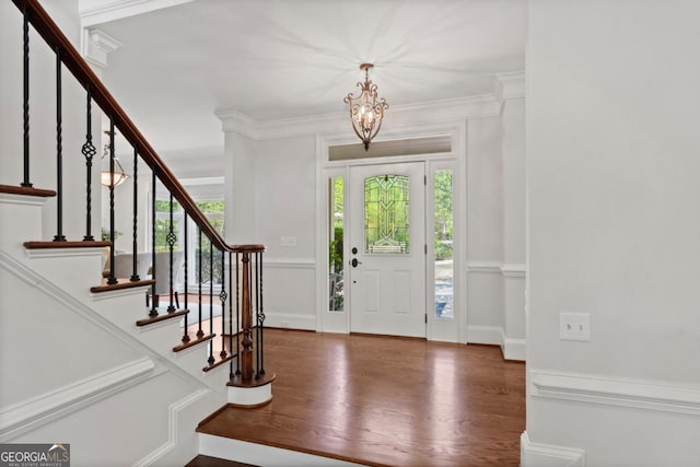 entryway with crown molding, wood finished floors, a notable chandelier, and stairway