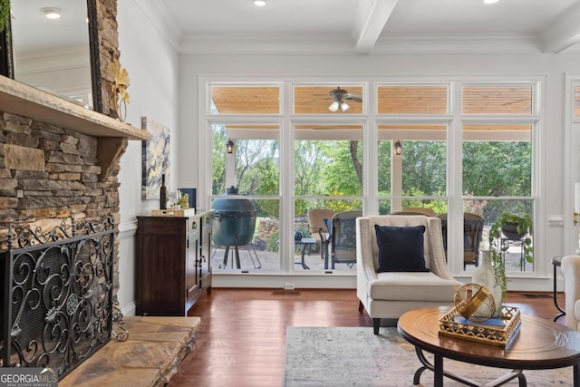 living room with ornamental molding, a stone fireplace, beamed ceiling, and dark wood-style floors