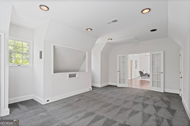 carpeted spare room with french doors, visible vents, attic access, and lofted ceiling
