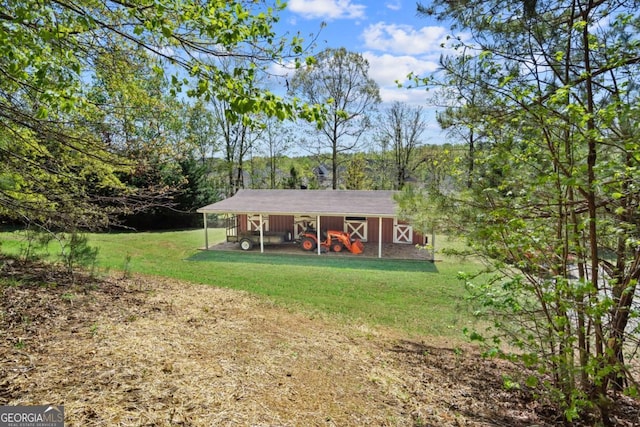 view of front facade featuring a front yard, a wooded view, an attached carport, and an outbuilding