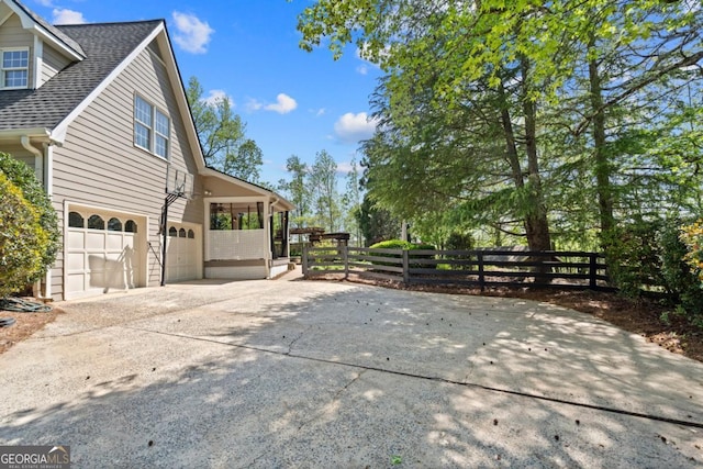view of side of home featuring roof with shingles, driveway, fence, and an attached garage