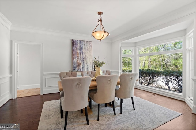 dining area featuring crown molding, a decorative wall, and wood finished floors