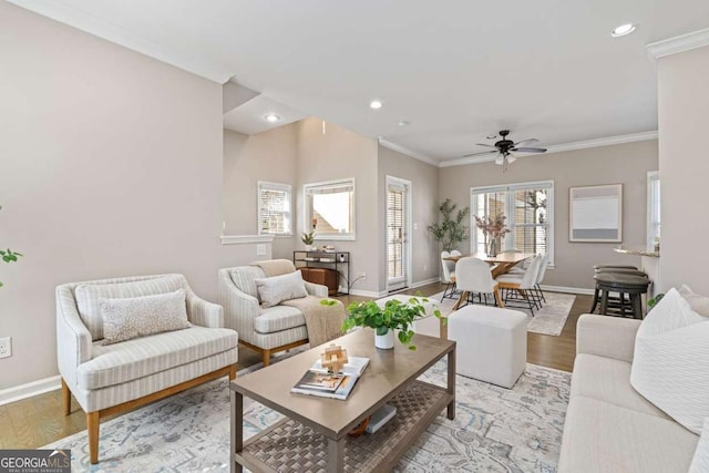living area featuring light wood-type flooring, crown molding, baseboards, and a ceiling fan