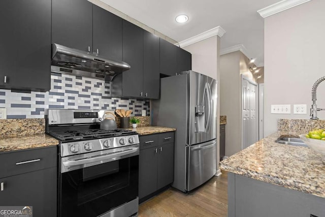 kitchen with crown molding, under cabinet range hood, a sink, stainless steel appliances, and light wood finished floors