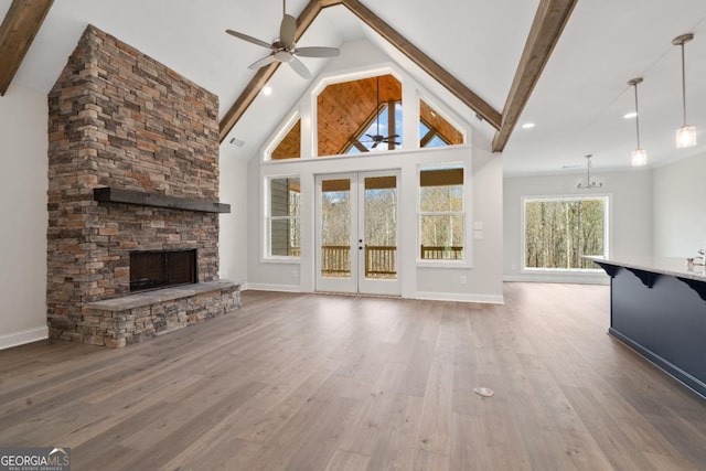 unfurnished living room featuring beam ceiling, a stone fireplace, wood finished floors, and ceiling fan with notable chandelier