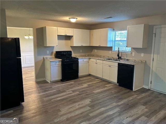 kitchen with a textured ceiling, a sink, visible vents, black appliances, and dark wood finished floors