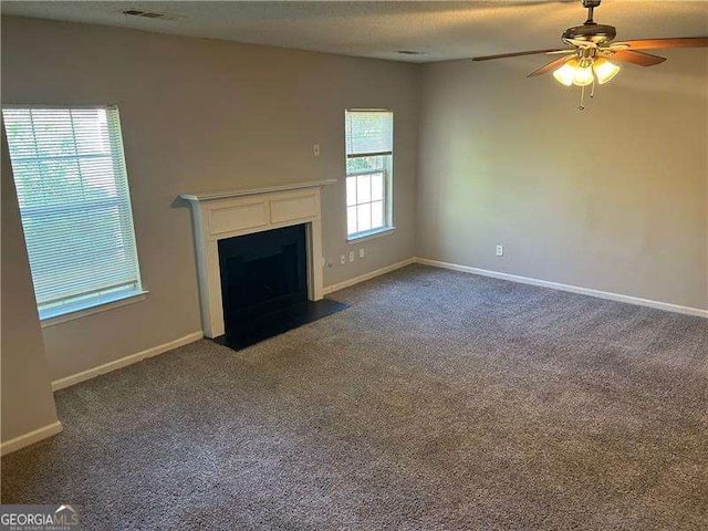 unfurnished living room with visible vents, dark carpet, ceiling fan, and a fireplace with flush hearth