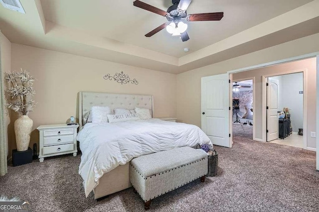 carpeted bedroom with a tray ceiling, ceiling fan, visible vents, and baseboards