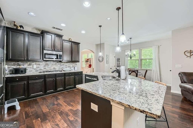 kitchen with light stone countertops, visible vents, decorative backsplash, arched walkways, and appliances with stainless steel finishes