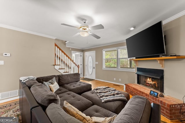 living area featuring ornamental molding, a ceiling fan, stairs, light wood-style floors, and a fireplace