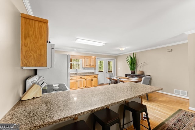 kitchen featuring a peninsula, electric range oven, a kitchen breakfast bar, ornamental molding, and light wood-type flooring