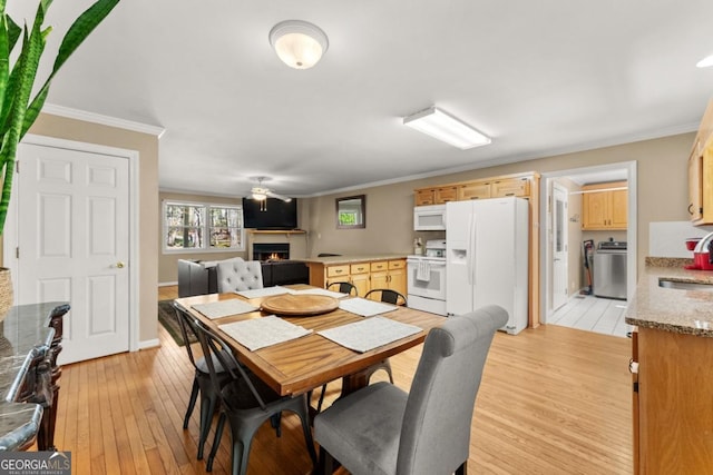 dining space featuring a lit fireplace, crown molding, light wood-type flooring, washer / dryer, and baseboards