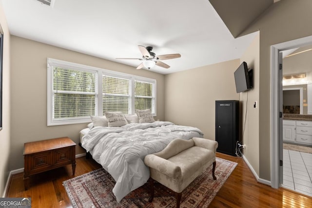 bedroom with wood finished floors, baseboards, ensuite bath, and ceiling fan