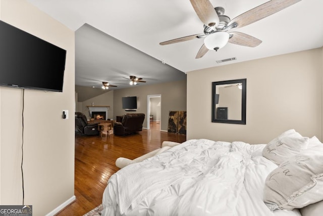 bedroom featuring a warm lit fireplace and wood finished floors