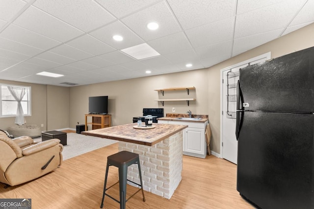 kitchen featuring freestanding refrigerator, a drop ceiling, light wood-style flooring, white cabinets, and a center island