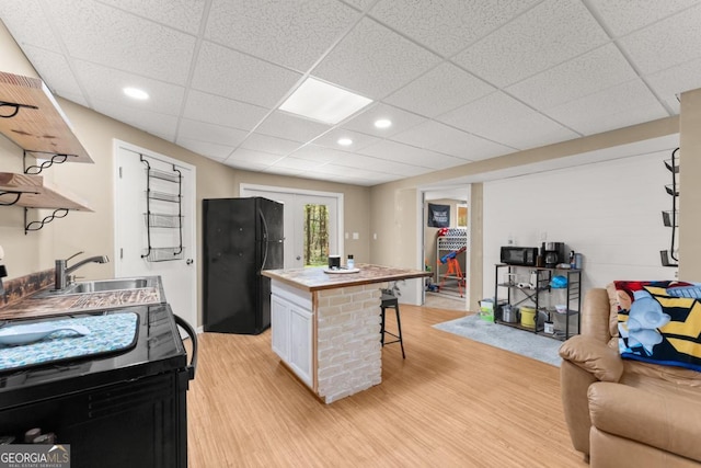 kitchen featuring freestanding refrigerator, open shelves, a sink, a breakfast bar, and light wood finished floors