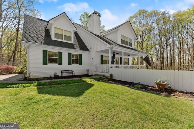 rear view of property featuring covered porch, a chimney, and roof with shingles