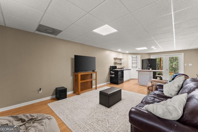 living area with a drop ceiling, light wood-style flooring, baseboards, and french doors