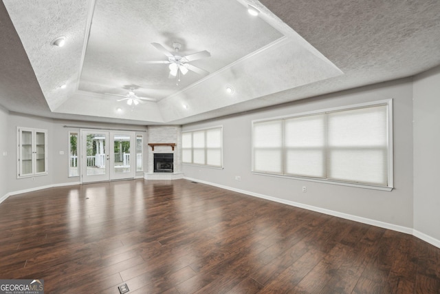 unfurnished living room featuring baseboards, ceiling fan, a textured ceiling, a tray ceiling, and wood-type flooring