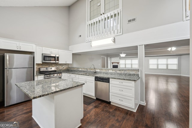kitchen with stone countertops, tasteful backsplash, a towering ceiling, appliances with stainless steel finishes, and a sink