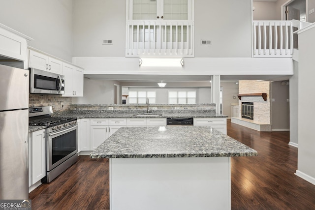 kitchen with a high ceiling, white cabinets, decorative backsplash, stainless steel appliances, and a sink